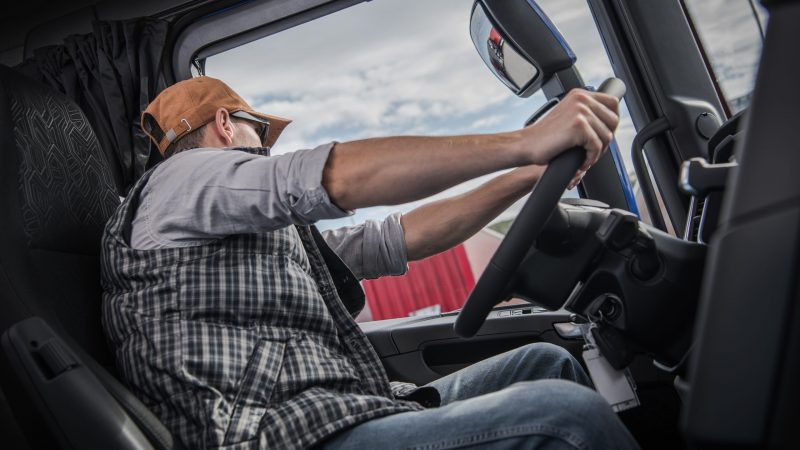 Caucasian Trucker in His 30s Behind Modern Semi Truck Wheel. Transportation Industry.