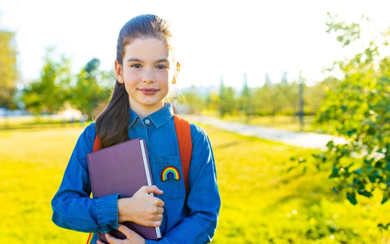Smiling indian student girl wearing school backpack and blue t-shirt in park .